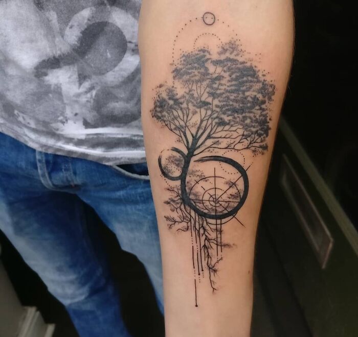 Forearm with a tattoo combining geometric shapes and a tree design, showcasing creativity and form.
