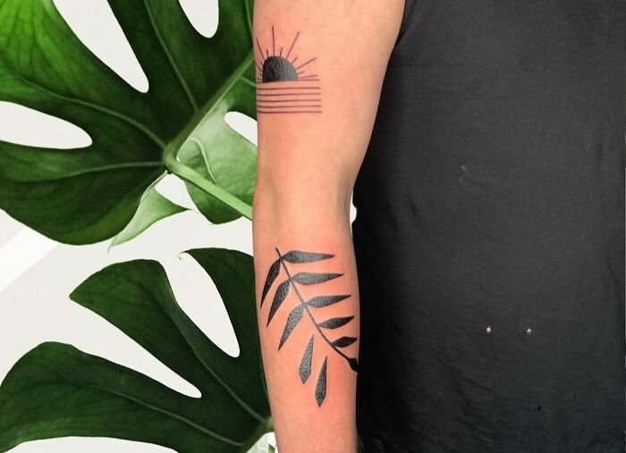 Geometric tattoo featuring a black sun and leaf design on an arm against a background of large green leaves.