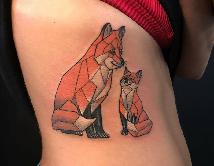 Geometric tattoo of two stylized foxes on a person's side, showcasing intricate design with sharp lines and bold colors.