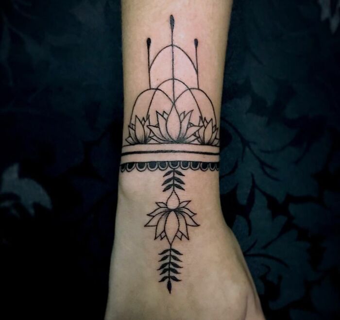 Geometric tattoo featuring lotus flower and symmetrical lines on forearm.