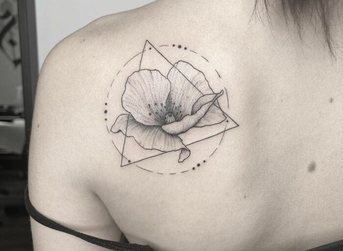 Geometric tattoo on shoulder featuring flower within triangle and circle design.