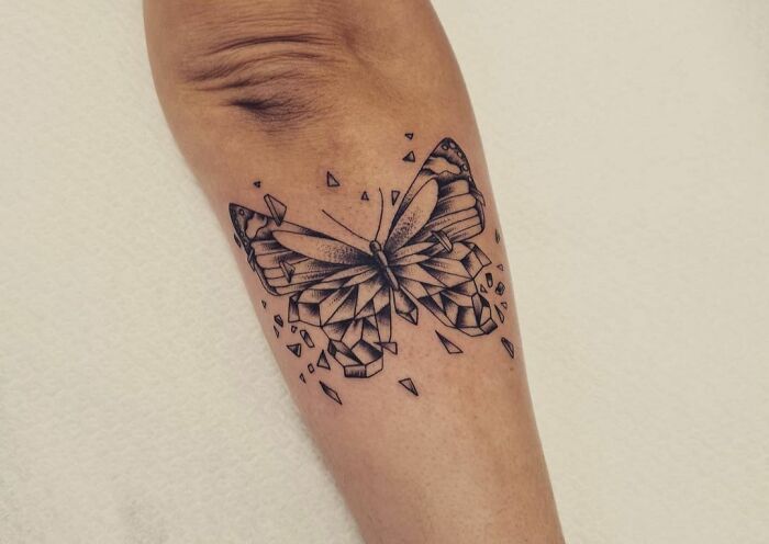 Geometric tattoo of a butterfly with fragmented shapes and creative patterns on a person's arm.