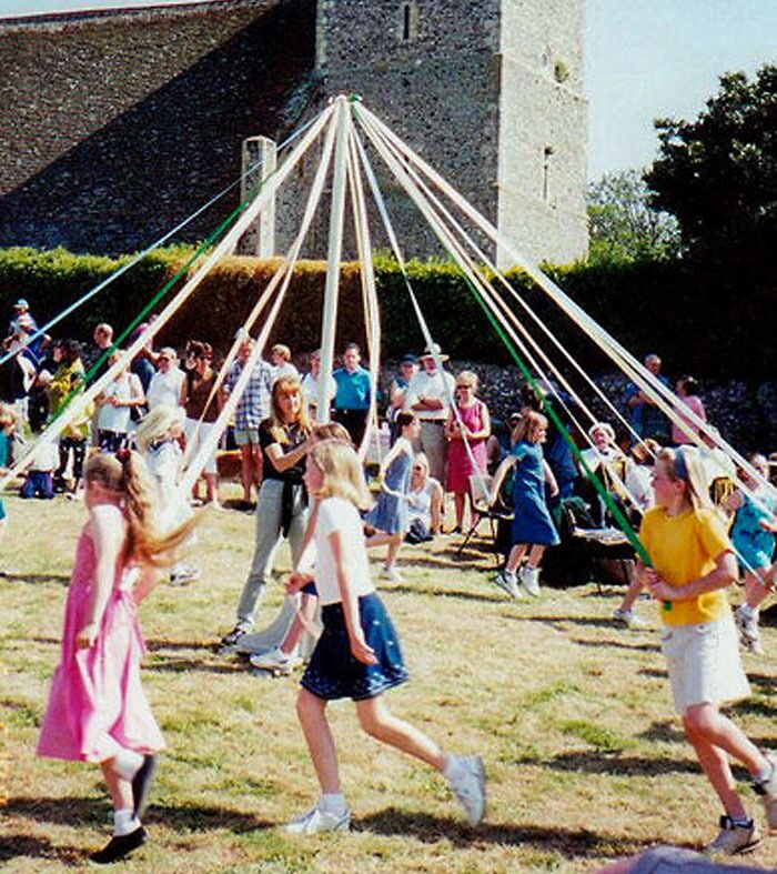 Maypole dancing with the tower of Bishopstone Church behind at Sussex