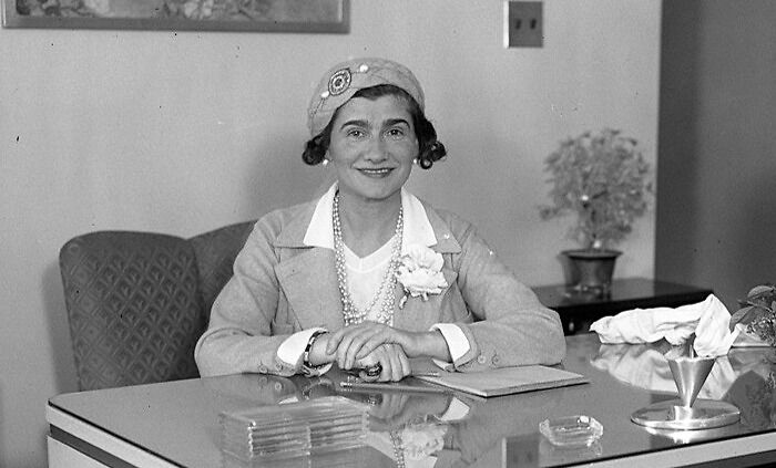 Coco Chanel smiling while seated at a desk, representing celebrities who never married yet still found love.