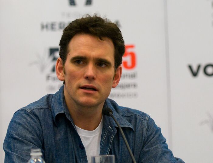 Matt Dillon wearing a white t-shirt and denim shirt speaking at an event about celebrities who never married yet found love