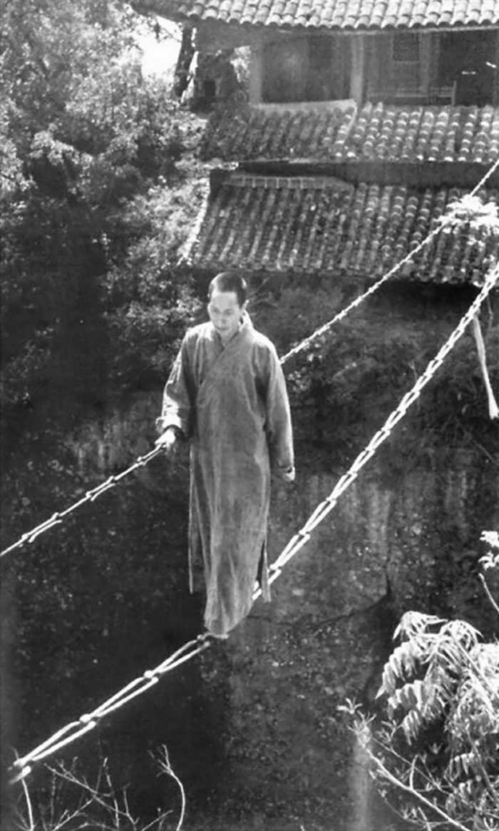 1930. Un monje budista chino camina sobre un puente de cadenas en el templo Jiangyou Figure Hill en China