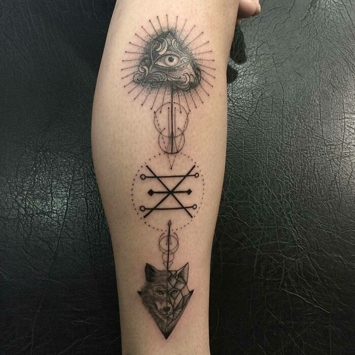 Geometric tattoo on forearm featuring an eye, abstract symbols, and a wolf design.