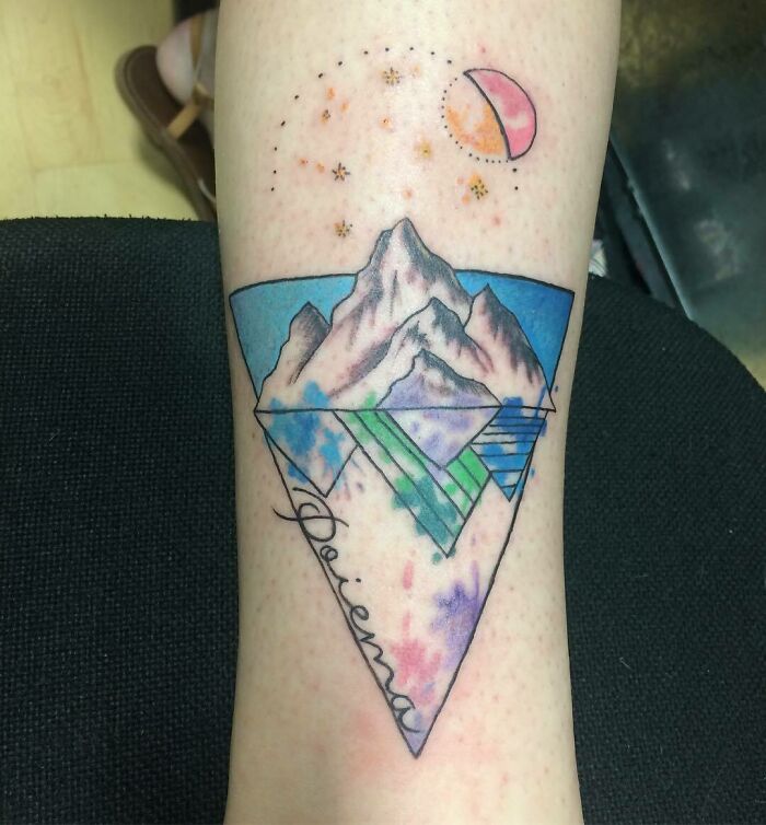 Geometric tattoo design on leg featuring mountains, moon, and abstract shapes in vibrant colors.