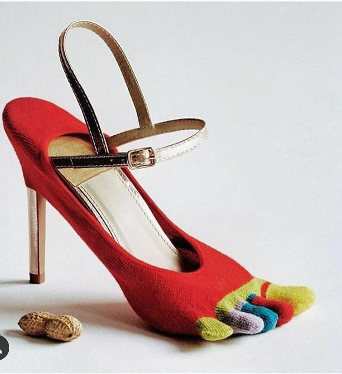 A weird shoe featuring a red high heel with colorful toe socks and a peanut nearby.