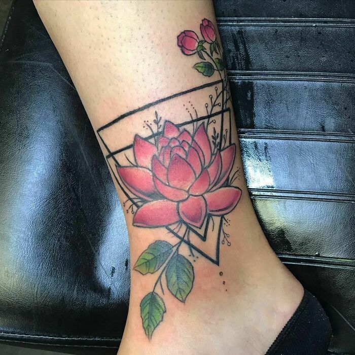 Geometric tattoo with a pink lotus and green leaves design on a person's leg.