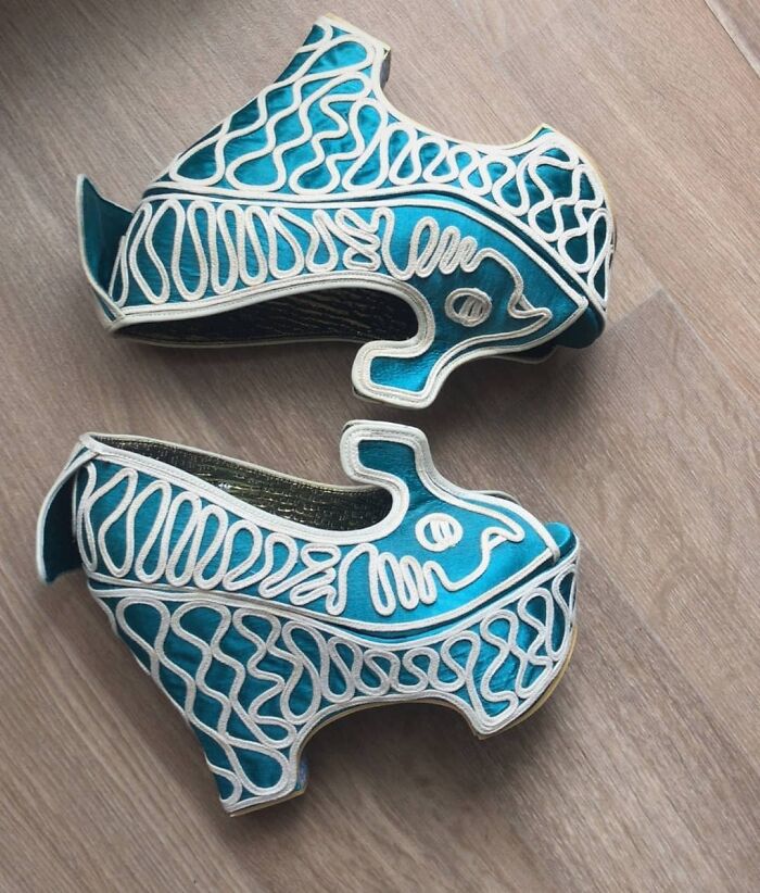 Weird shoes with intricate blue and white design resembling stylized horse shapes on a wooden floor.