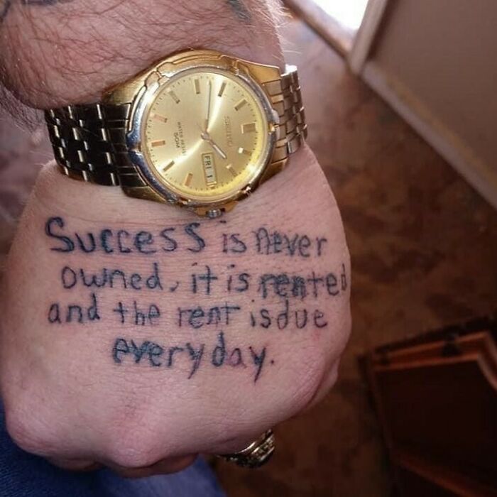 Tattoo reads "Success is never owned, it is rented," written on hand with a gold watch; example of horrible tattoos.