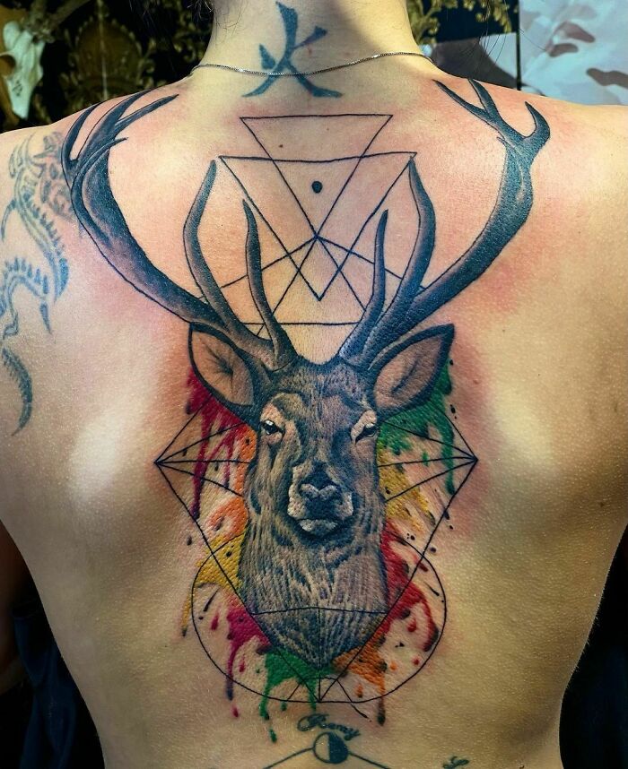 Geometric tattoo featuring a deer head with colorful accents and overlapping triangle designs on a person's back.