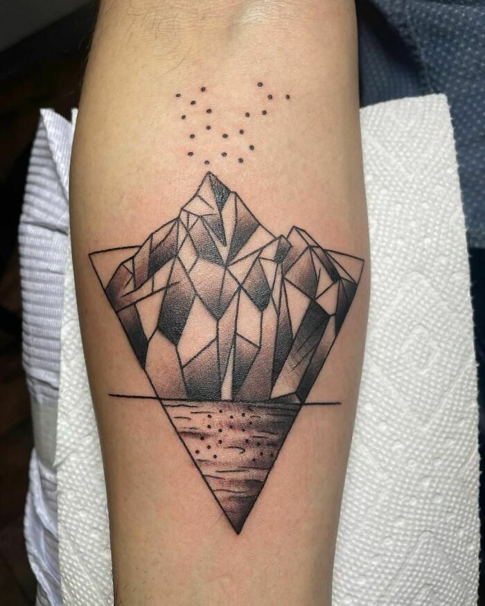 Geometric tattoo featuring a faceted mountain design with dot detailing above, inked on an arm.