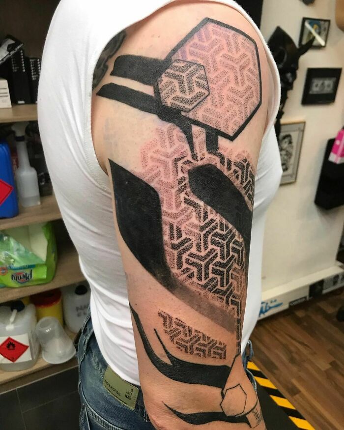Arm with a geometric tattoo featuring hexagonal patterns and bold black shapes.