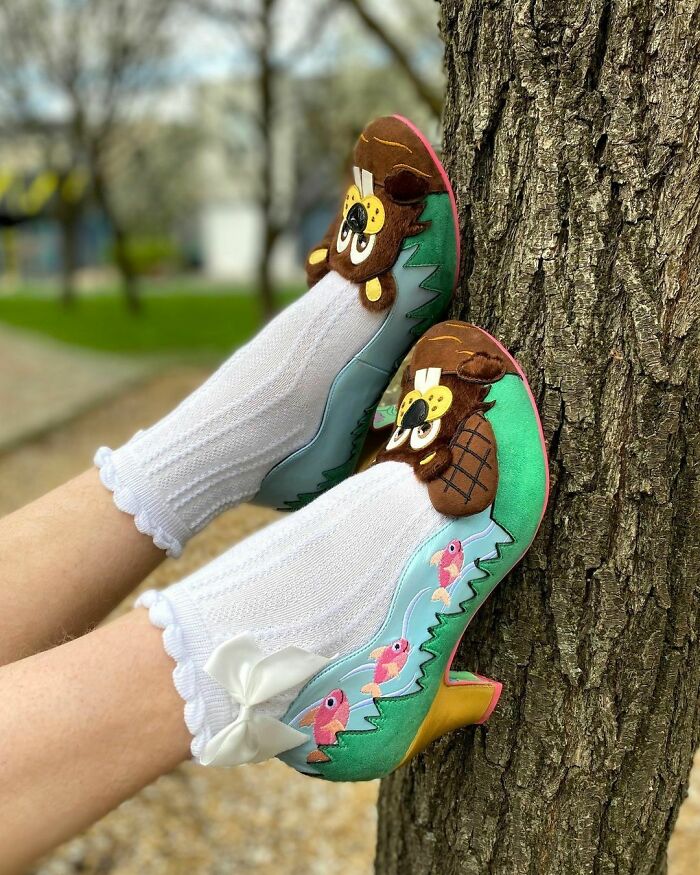 Weird shoes featuring playful owl and fish designs worn with white socks against a tree background.