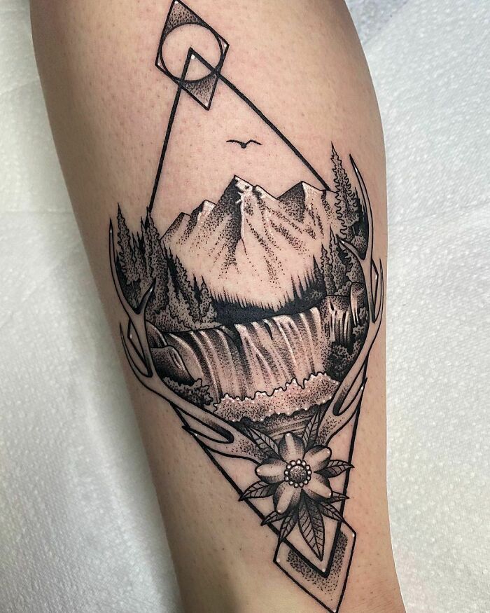Geometric tattoo featuring mountains, waterfall, and floral details with angular shapes.