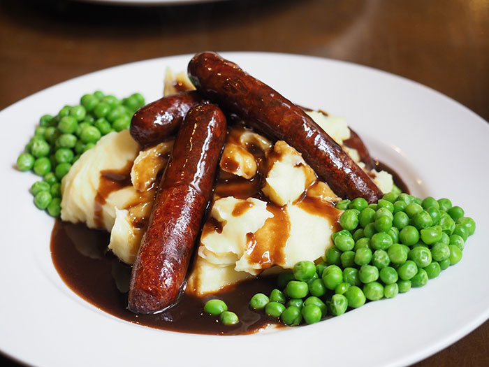 Sausages, mashed potatoes, peas and gravy in a white plate 