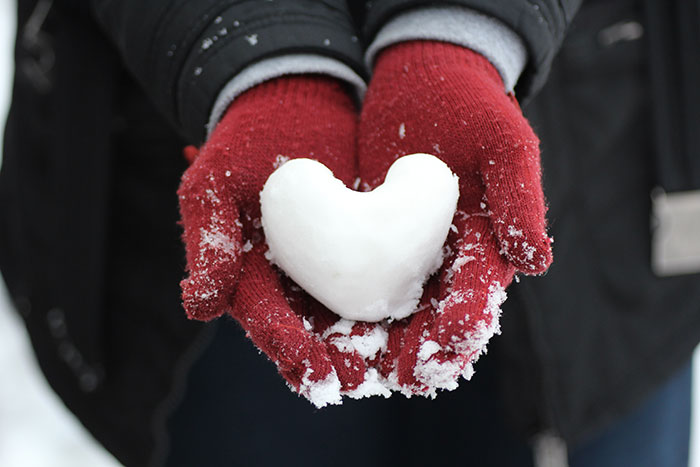Person holding heart shaped snow in hands