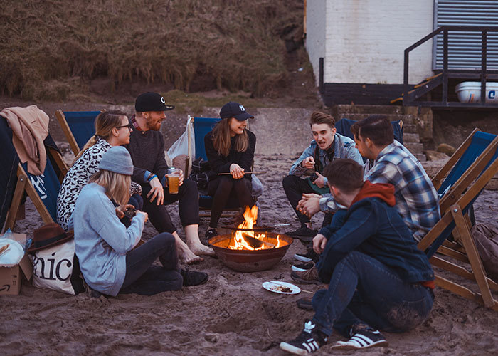 Group of friends talking on beach near a fire pit 