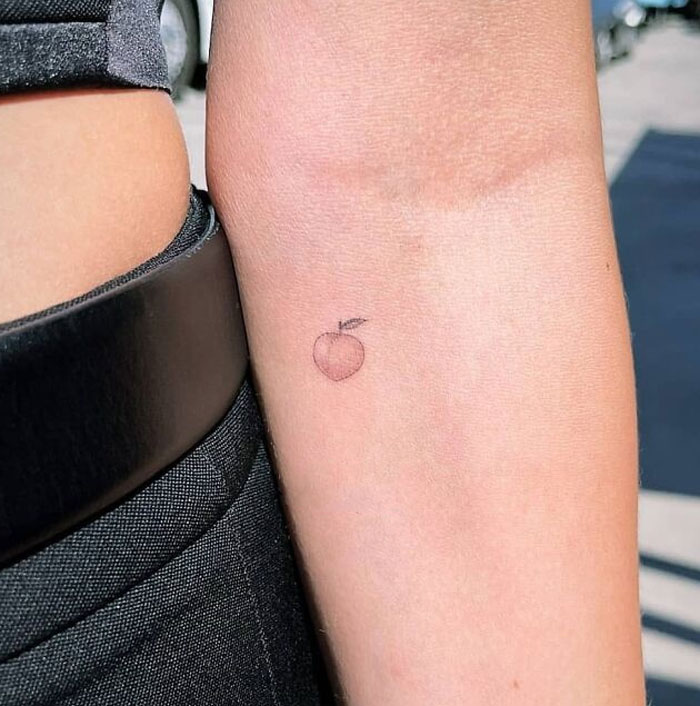 Celebrity tattoo of a small peach on the inner arm.