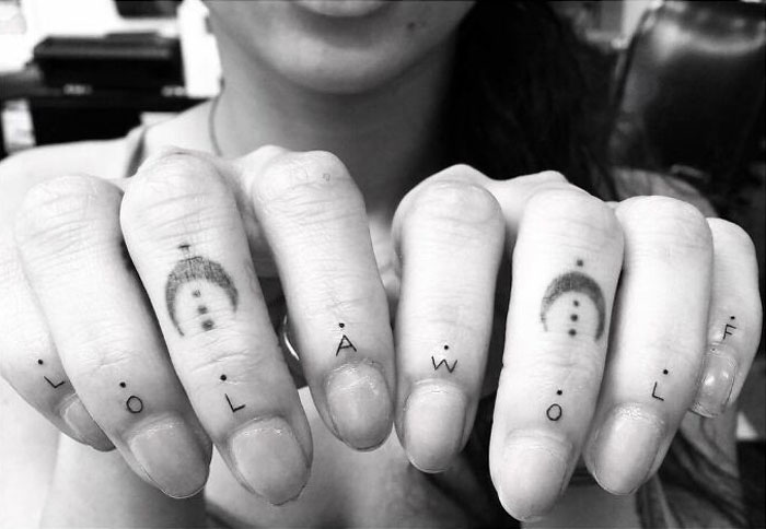 Celebrity tattoos on fingers spelling "LOL AWOLF" in black ink, showcasing a minimalist style.