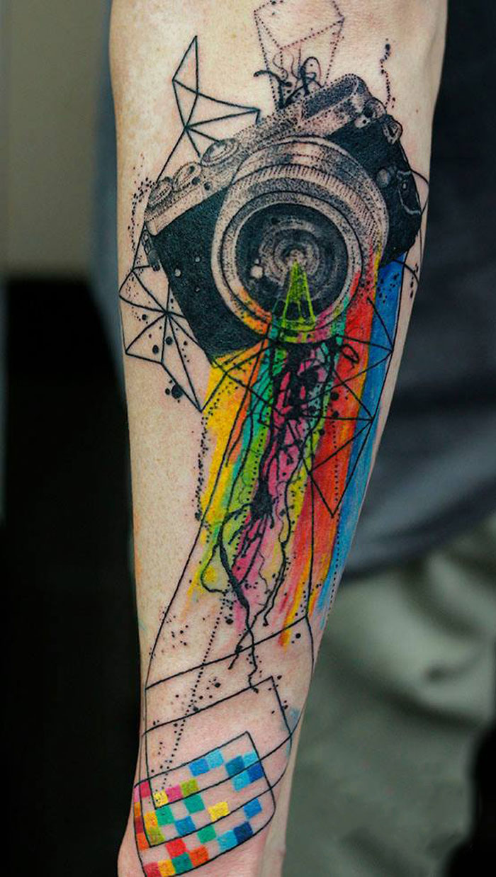 Geometric tattoo with a colorful camera design and abstract shapes on an arm.