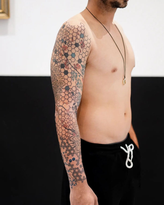 Man displaying a sleeve of exquisite geometric tattoos against a black and white background.