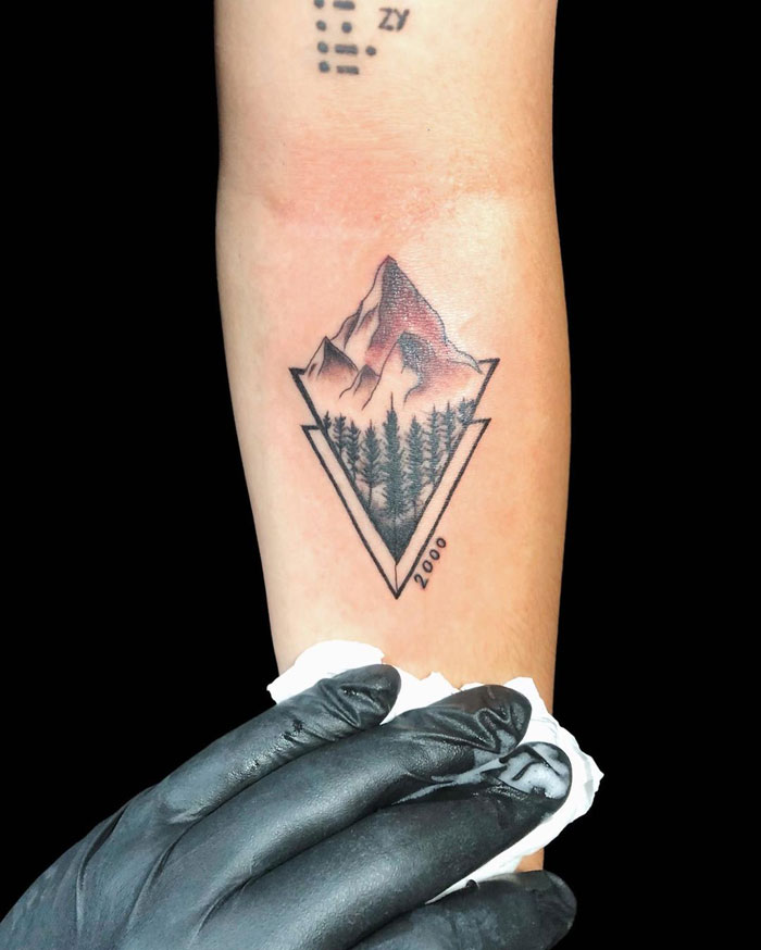 Geometric tattoo design featuring mountains and trees inside a triangle on an arm.