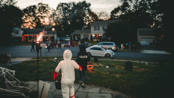 Kids dressed in Halloween costumes going Trick-or-treating in a neighborhood at evening