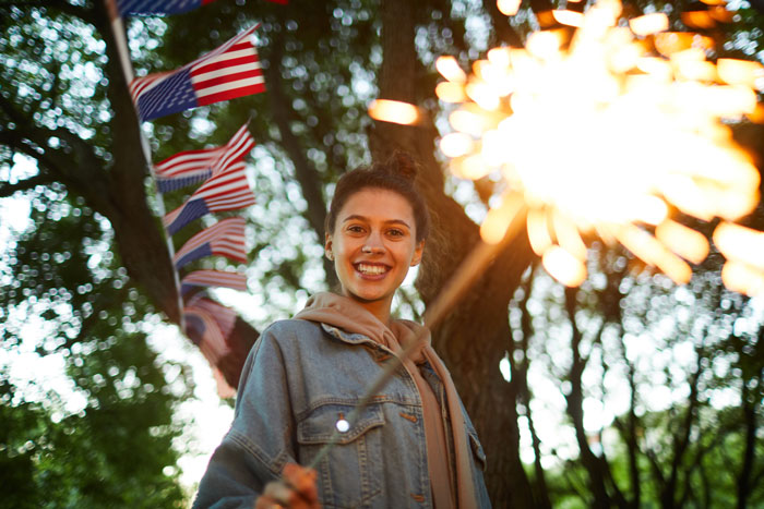 Smiling woman holding a sparkler in the background of hung up American flags