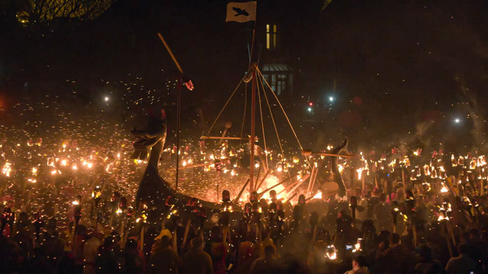 Crowd of people holding torches near big Viking ship at Up Helly Aa Fire Festival 