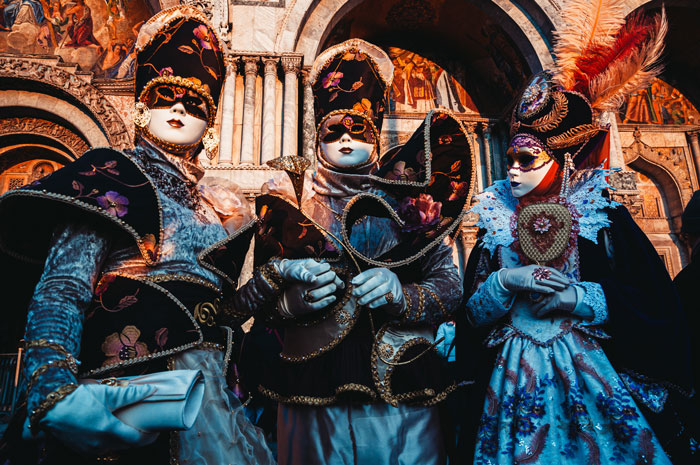 Three people dressed in Venetian carnival costumes and masks