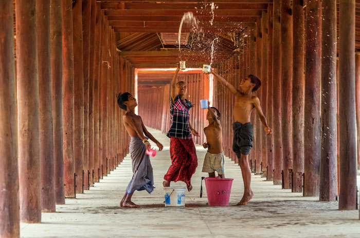 Four kids spilling water over their heads in a wooden tunnel