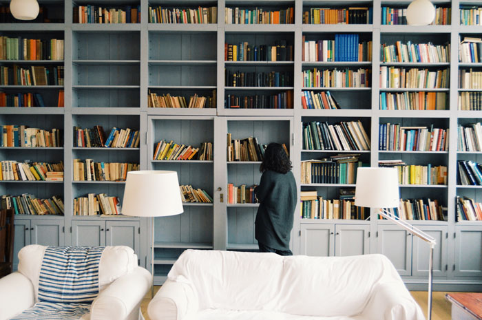 Woman organizing books on large home library shelves.