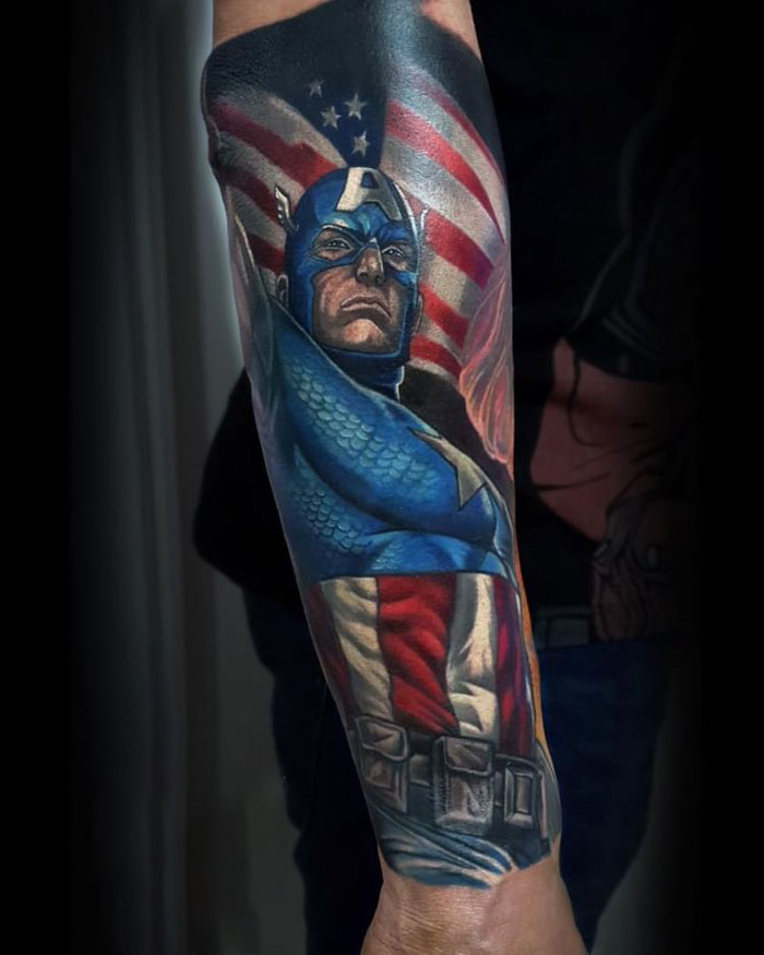Colorful Marvel tattoo on forearm featuring Captain America with shield and American flag in background.