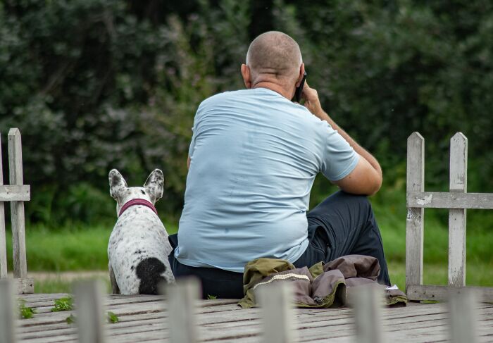 Man Sitting With His Dog And Talking On His Phone 