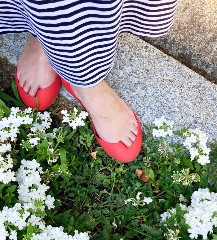 Feet in red weird shoes on a grass path surrounded by small white flowers.