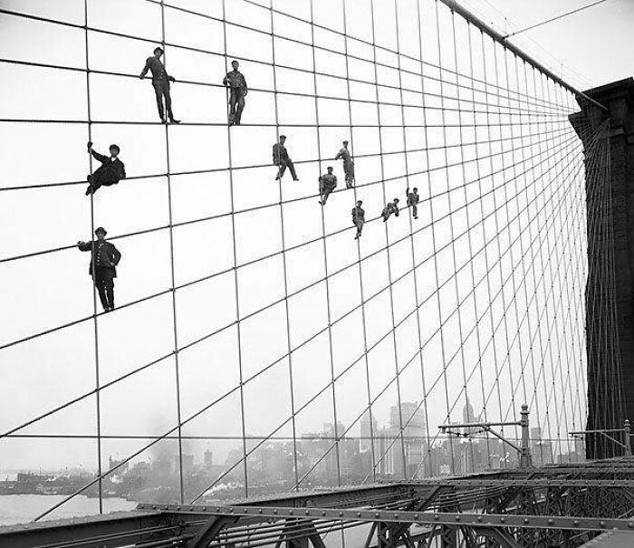 Hombres posando sobre los cables de acero del puente de Brooklyn
