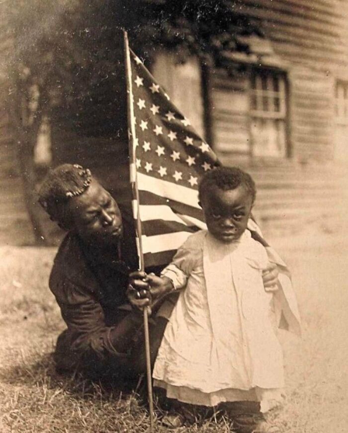 Una madre y su hija sostienen la bandera estadounidense a principios del siglo XX