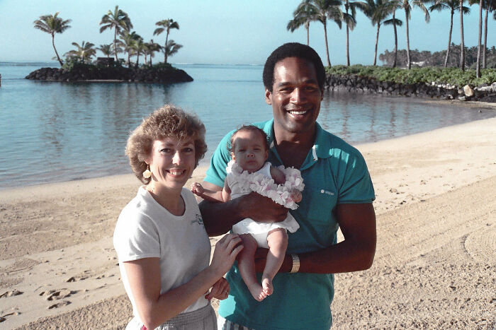 A cheerful couple with a baby at a tropical beach; linked to celebrities and crimes.