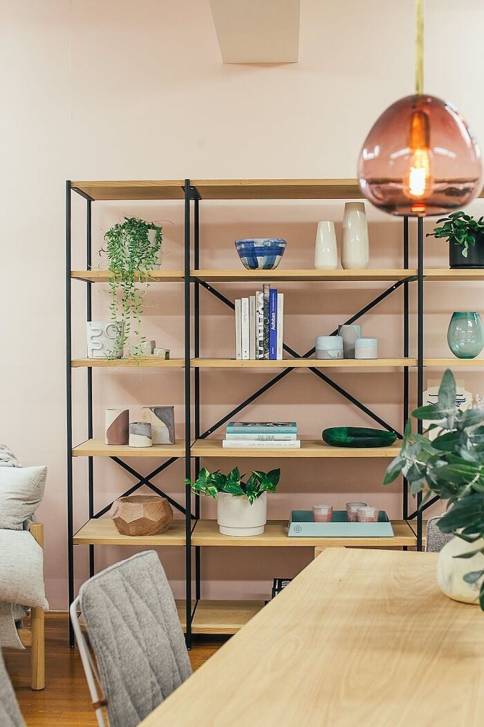 Home organization idea with neatly arranged books and decor on a modern shelf against a pink wall.