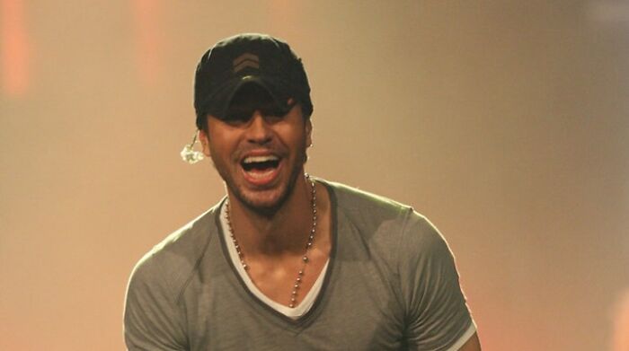 Enrique Iglesias wearing grey shirt and cap, smiling on stage, featured among celebrities who never married yet found love