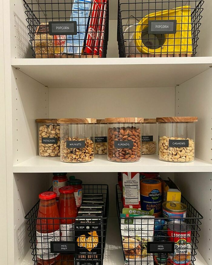 Home organization with labeled jars of nuts and wire baskets storing pantry items on white shelves.