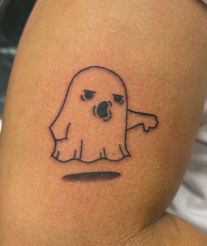 Funny tattoo of a cartoon ghost with an angry expression on arm skin.