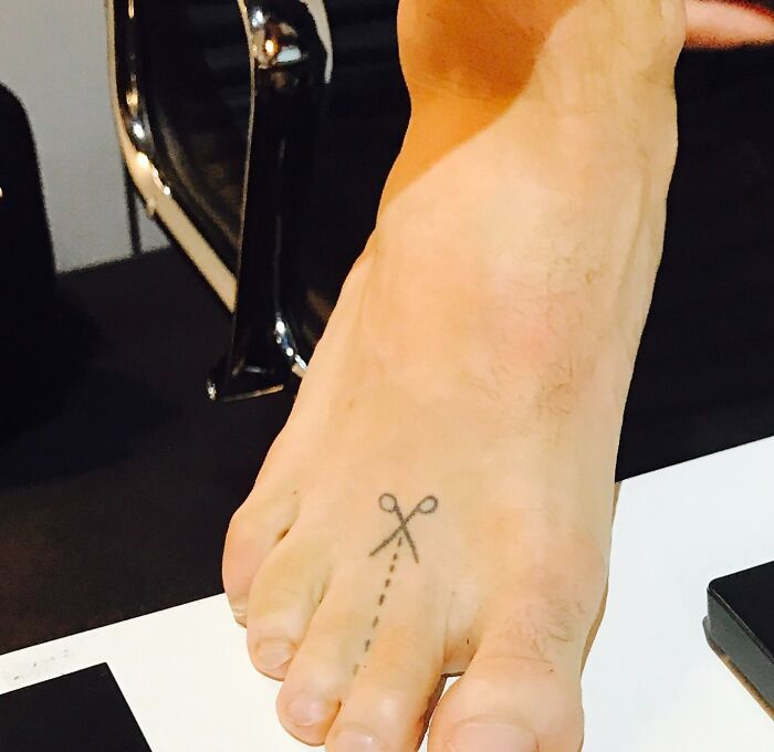 A funny tattoo of scissors and a dotted line on a foot.