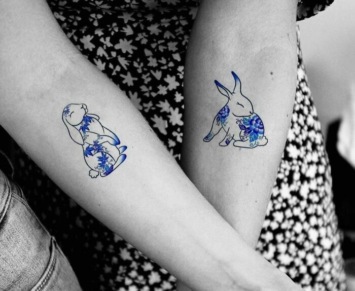 Two arms with matching blue floral bunny tattoos, symbolizing best friend tattoos.