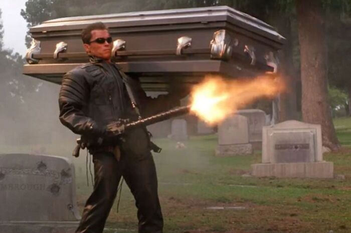 Action scene with a highest-paid actor firing a powerful weapon while wearing black leather in a graveyard setting.