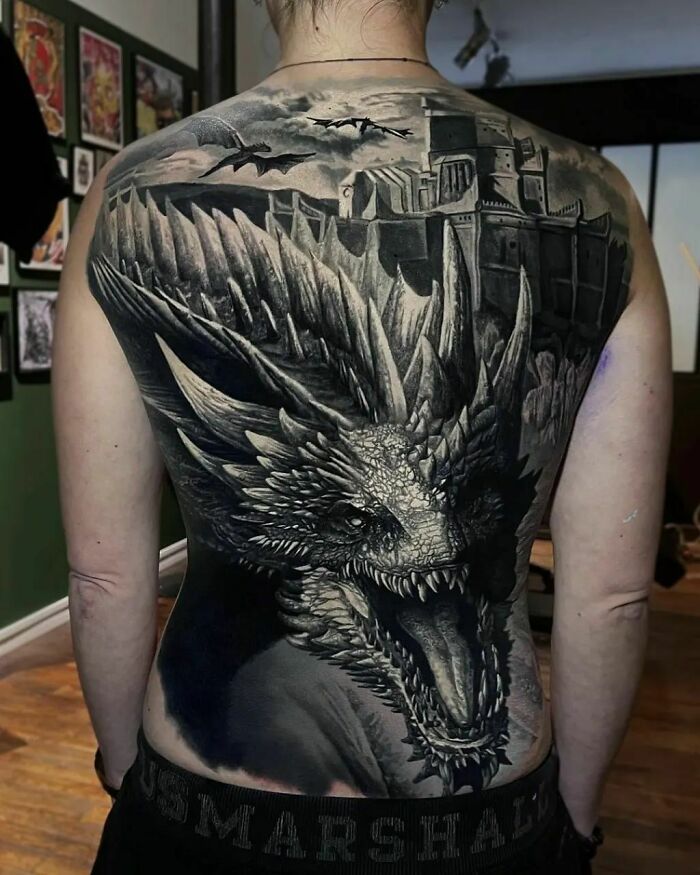 Super realistic tattoo featuring a detailed dragon and castle design, covering an entire back.