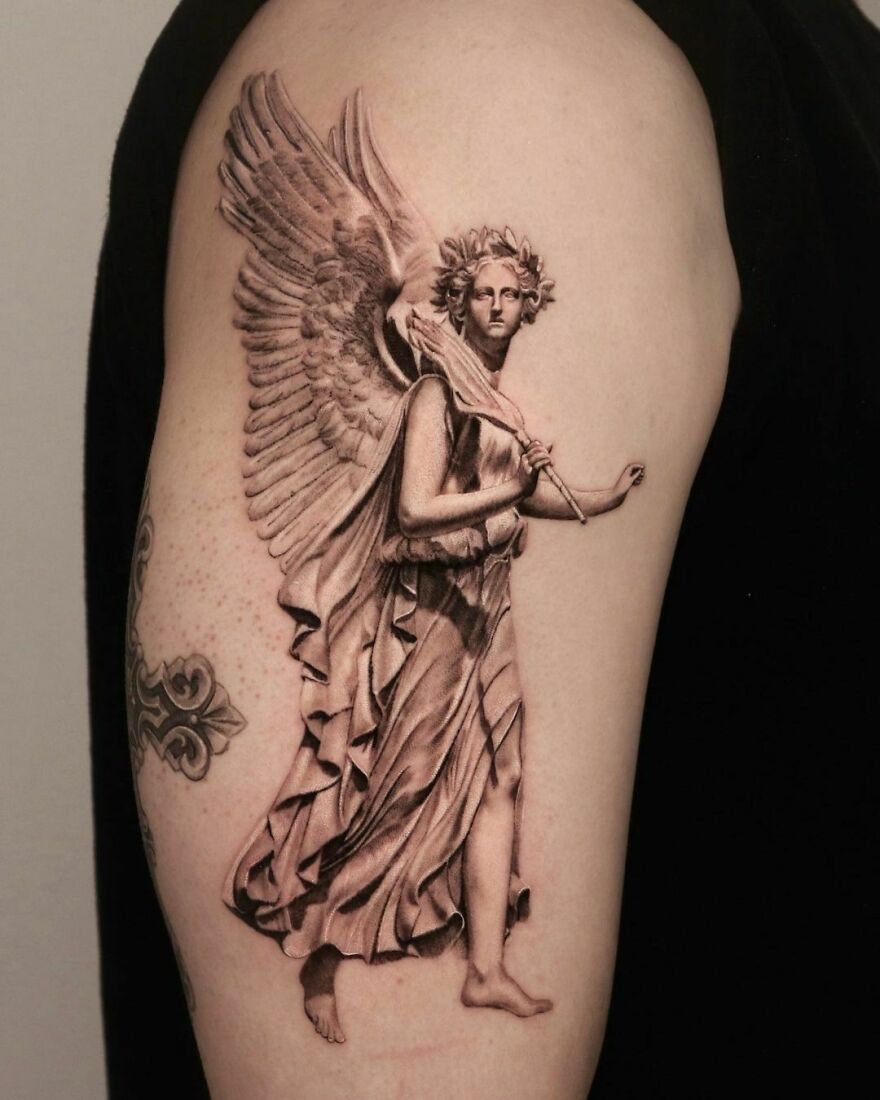Super realistic tattoo of the Goddess of Victory with detailed sculptural likeness and ethereal wings on arm.